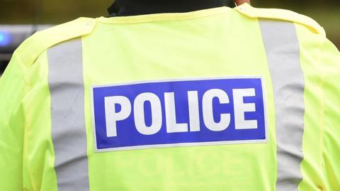 A police officer wearing a fluorescent jacket with POLICE in large white letters on a blue background