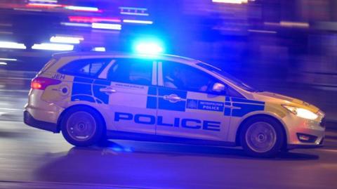 A generic image of a Metropolitan Police car driving quickly at night. 