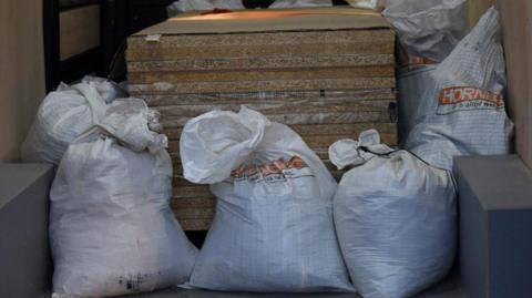 A number of large white sacks can be seen in the back of a van.