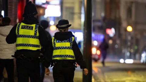 A male and female police officer in high vis tops with their backs to the camera, walking down a street at night in Bournemouth town centre 