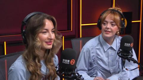 Holly and Lauren from Remember Monday sit in the ý Radio 2 studio. They are wearing light blue shirts and tops