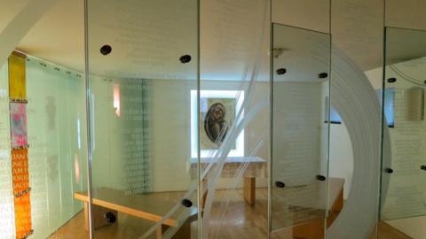 A transparent glass screen inside a chapel, with names etched on them vertically 