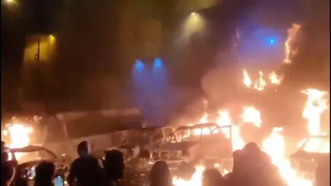 Protesters gather in front of burning vehicles in Tehran, Iran