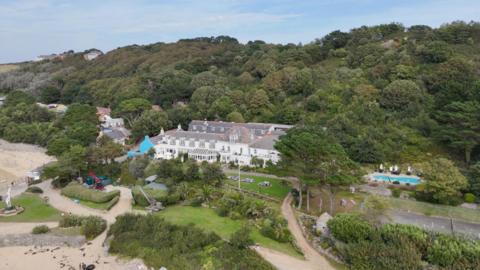 The White House Hotel on Herm. It is a large white building set back from the beach amongst trees and grass.