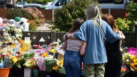 A woman and two children look at flowers laid at the scene of the Southport stabbings