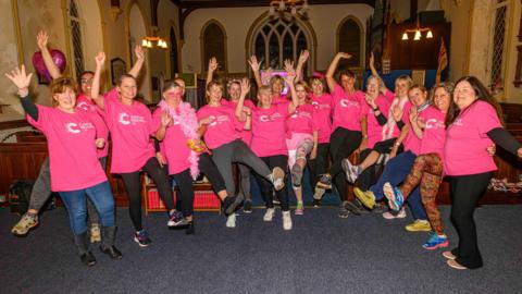 A group of women in pink t-shirts wave their arms in Arkengarthdale community hub