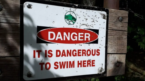 A white sign with red writing. The sign reads: "Danger. It is dangerous to swim here." 