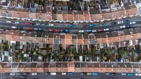 An aerial view shot of houses in Bristol. The roofs are different shades of brown and grey and cars and roads can be seen.