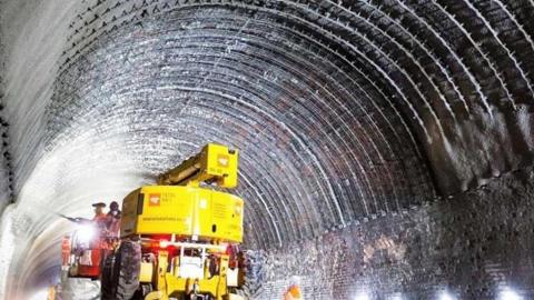 A piece of heavy machinery carrying out maintenance work inside a railway tunnel, being operated by workers in hi vis.