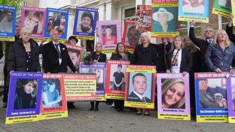 A group of relatives standing outside the Lampard Inquiry holding placards featuring the faces of loved ones, mostly featuring the phrase "Failed by the state"