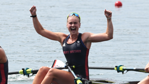 Hannah Scott celebrating with her arms in the air on a rowing boat. She is wearing a tank top with "Great Britain" written across the chest.