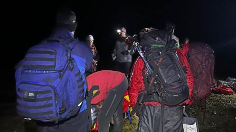 People in red and green jackets in the dark with helmets and torches on