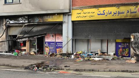 A burnt out shop following racist attacks on Sandy Row - bits of debris and burnt food lie on the pavement outside the shop 