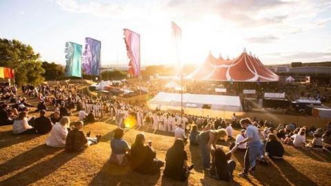 Crowds looking down a hill at a big tent at a festival.
