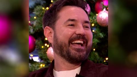 Martin Compston laughs in front of a decorated Christmas tree