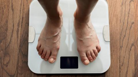 Top down view of feet standing on white digital bathroom scale over wooden floor