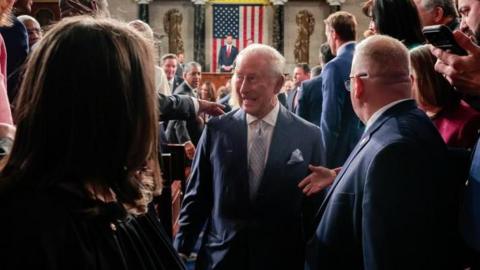 King Charles, with a grin on his face, walks by lawmakers in US Congress after delivering his speech, with US Vice-President JD Vance and a US flag visible distantly behind him