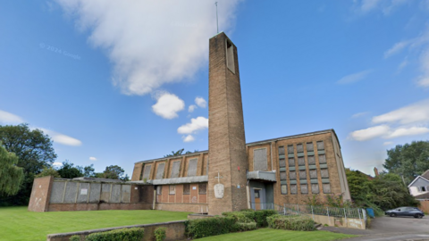 A 1950s-style brick church with a tall tower and a main building with boarded up windows