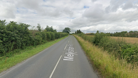 Google maps street view of Melksham Road in Holt, Wiltshire. There are fields and lots of green space on either side of the road.