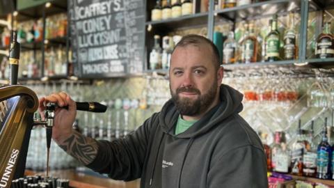 Christopher Rawlinson is standing behind the bar, pulling a pint of stout