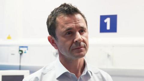 A man with short brown hair wearing a white suit shirt.