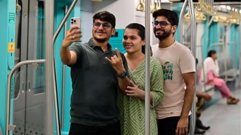 Three people take a selfie together on a metro train in India