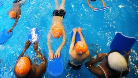 Swimmers use floats an have swimming hats on in a leisure centre pool