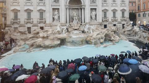 Tourists stand and look on at the Trevi Fountain