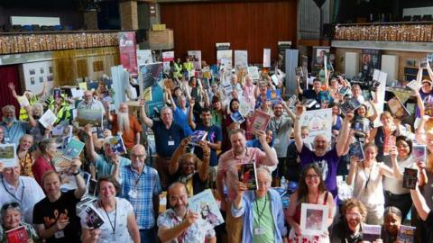 A group of authors smiling while posing for a photo, raising their books.