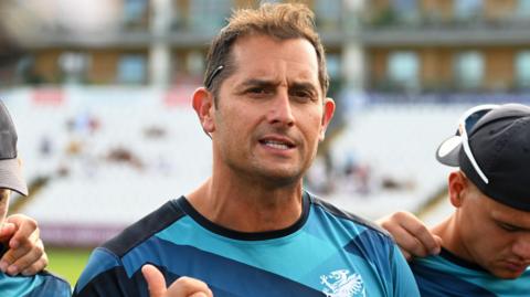 Jason Kerr, wearing a Somerset training top with navy blue, blue and light blue patterns and a white Somerset badge, while talking to his players before a T20 game against Glamorgan at the County Ground