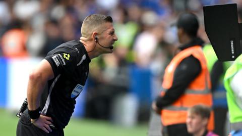 Referee Robert Jones reviews Josh King's goal on the pitchside VAR monitor
