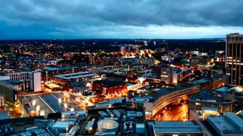 Birmingham at night with streets and buildings lit up by lights under grey clouds.