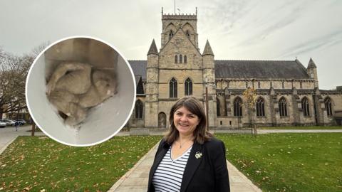 Emma Lingard stands infront of Grimsby Minster with a cutout of 'The Grimsby Imp' next to her