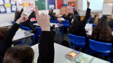 Pupils raise their hands in a lesson.