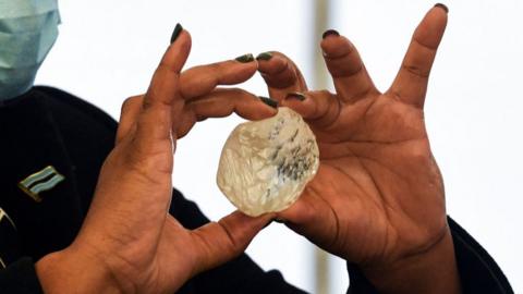 A woman with painted nails holds a large diamond