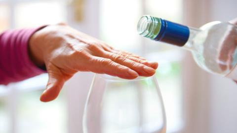 A hand covers a glass while another hand hovers over with a wine bottle