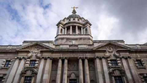 The outside of the Old Bailey court, a large grey building with a golden statue on top