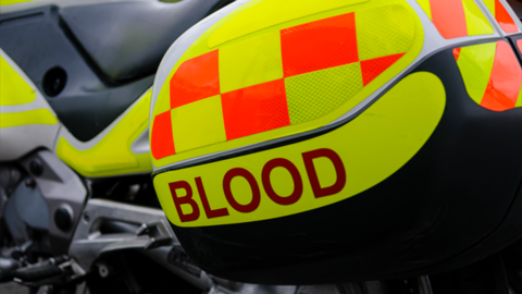 A close up of a motorcycle, with a compartment that says blood on it in red lettering. The motorcycle is a blood blike, and is yellow with orange squares on it.