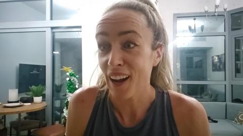 Eilish McColgan - seated at a desk, in the middle of talking on a web call with a couch and plants visible behind her