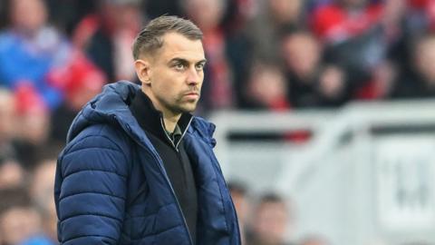 Southampton head coach Tonda Eckert wearing a navy puffer jacket looks into the distance 