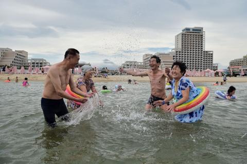 North Koreans splash in the water by the beach lined with hotels on an overcast day