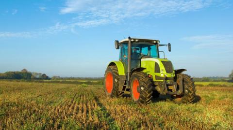 A green tractor with large red wheels parked in a field