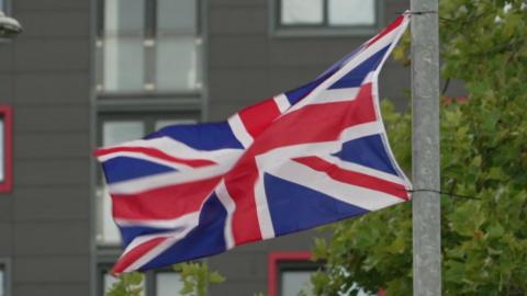 A union jack flying from a grey metal lamppost 