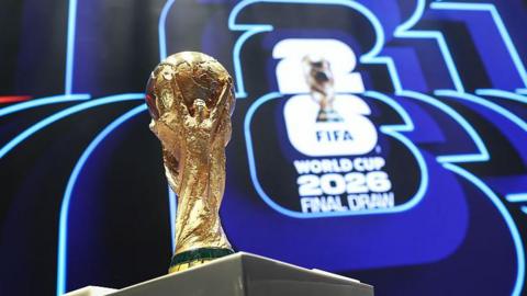 The World Cup trophy in front of the logo for the 2026 World Cup