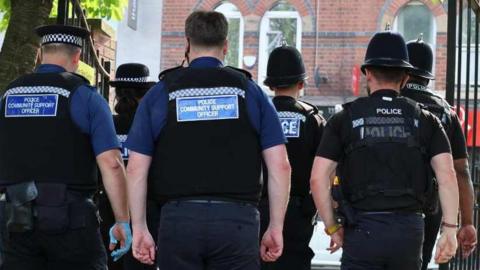 A group of police community support officers and police officers walking together. The image shows the backs of the officers walking away. 