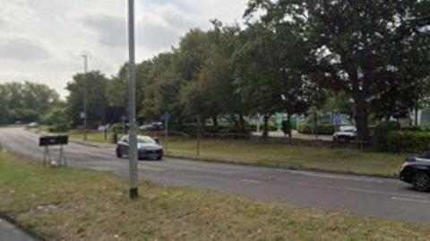 A view of part of Rowley Lane shows cars on a dual carriageway with trees and industrial buildings in the background