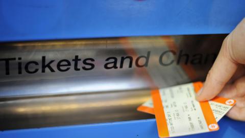 A picture of tickets being printed at a train station. There are two orange tickets being taken out of the machine.