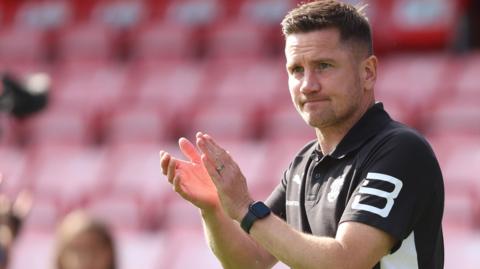 Crewe manager Lee Bell claps the fans in his black and white club polo shirt at the end of 3-1 win at Salford