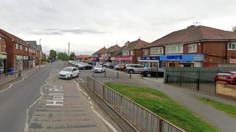 A Google Street View image of Hull Road, featuring rows of shops in the village centre