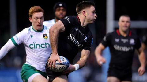 Fergus Burke of Saracens passes the ball